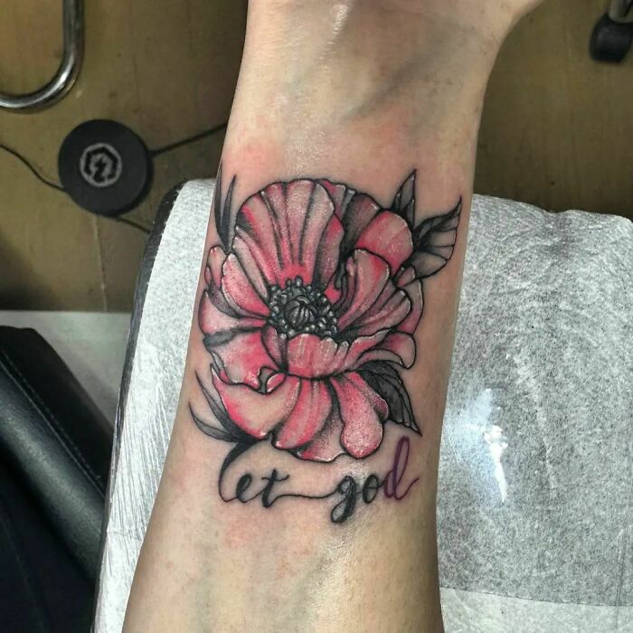 Pink flower tattoo with black leaves and the phrase "let go" on forearm, showcasing vibrant blossom design.