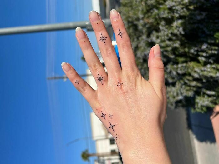 Hand with minimalist space tattoos featuring stars and sparkles, perfect for astrology fans.
