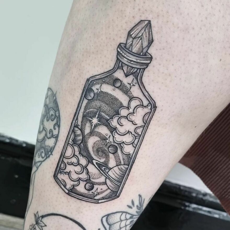 Space tattoo depicting planets and clouds in a bottle on a person's arm.