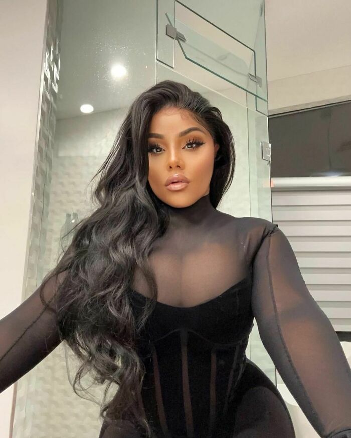 "A celebrity wearing a black sheer outfit poses in a modern interior setting."