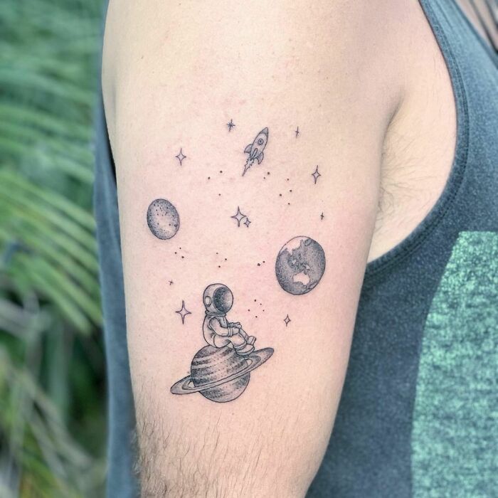 Astronaut sitting on Saturn tattoo, featuring planets and a rocket, perfect for astrology enthusiasts.