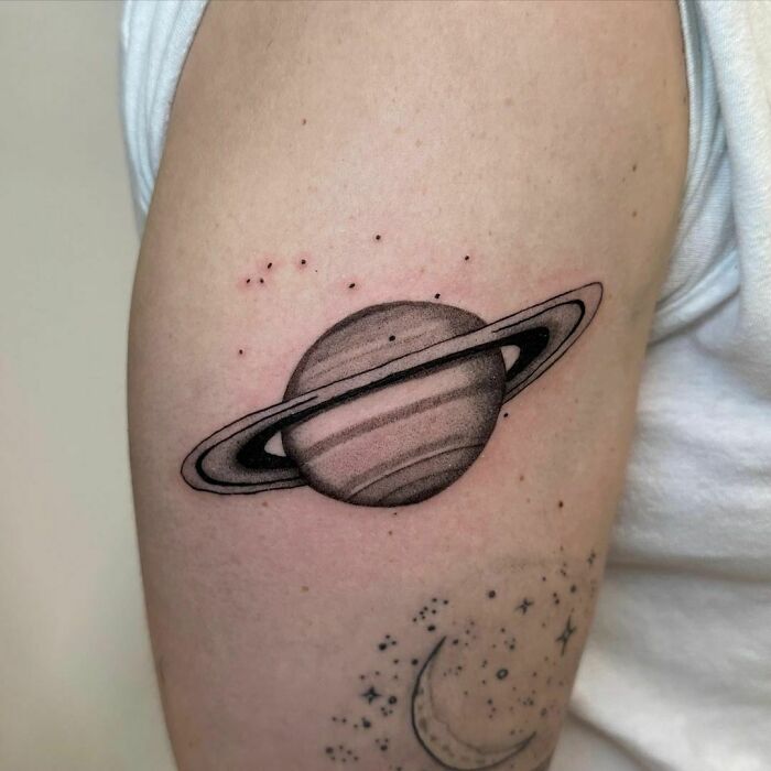 Astrology tattoo featuring Saturn and stars on an upper arm.