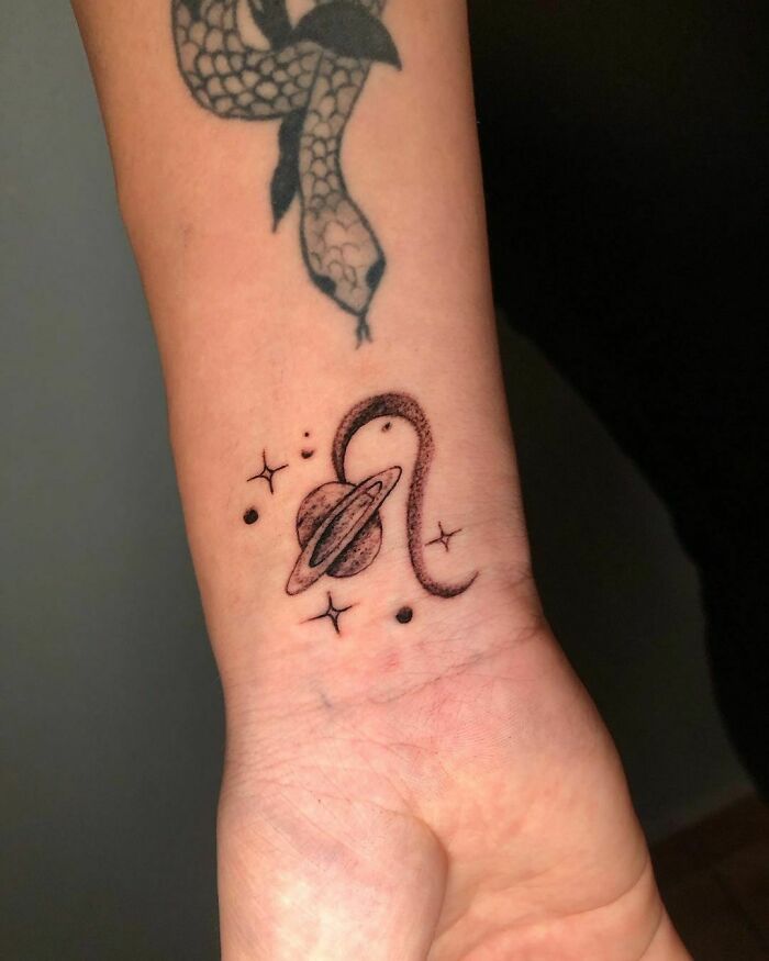 Astrology-themed space tattoo featuring a planet with a ring and stars on a person's wrist.