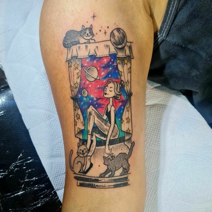 Space tattoo with a woman gazing at planets through a colorful window, surrounded by cats.