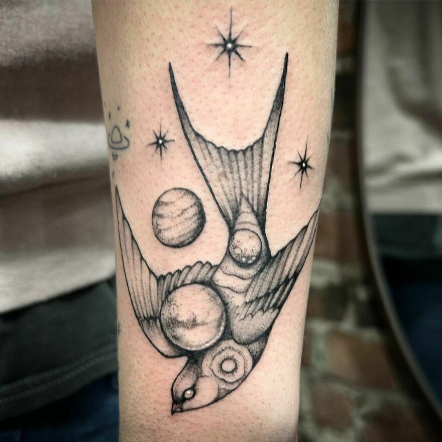 Tattoo of a bird with planets and stars, showcasing an outer space themed design.