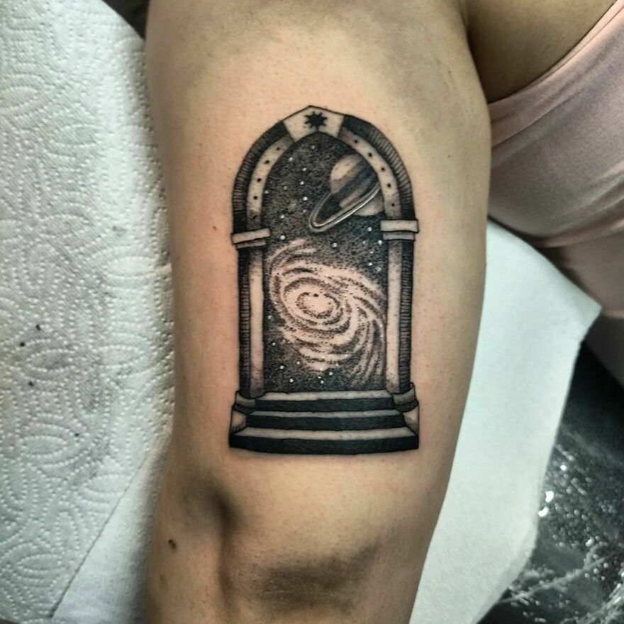 Space tattoo of a galaxy and Saturn framed in an arch on arm.