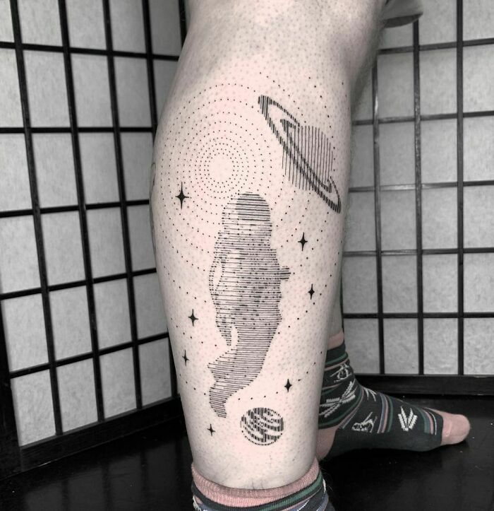 Space tattoo with an astronaut, planet, and stars on a leg, showcasing cosmic-themed art.