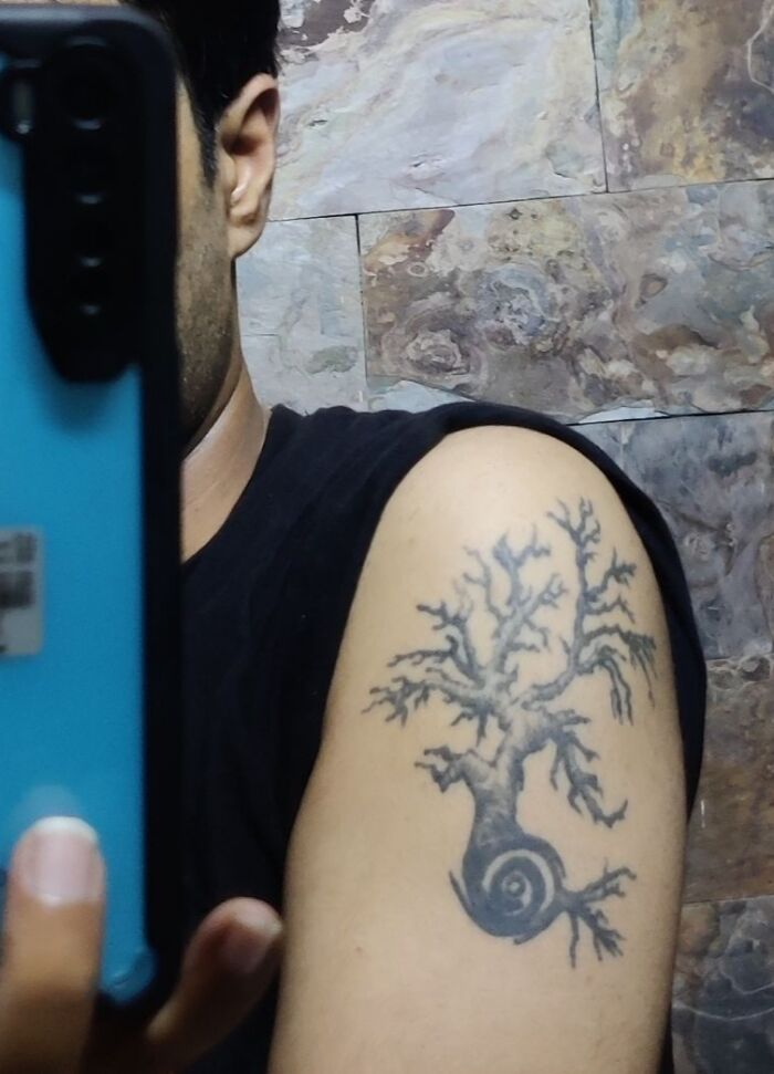 Close-up of an arm with a tree tattoo featuring intricate branches, taken in a bathroom setting.
