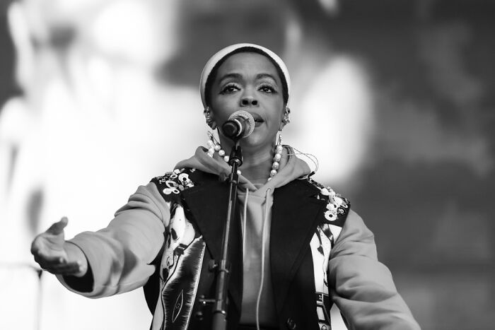 Celebrity singing on stage with a microphone, wearing a decorated jacket and headband.
