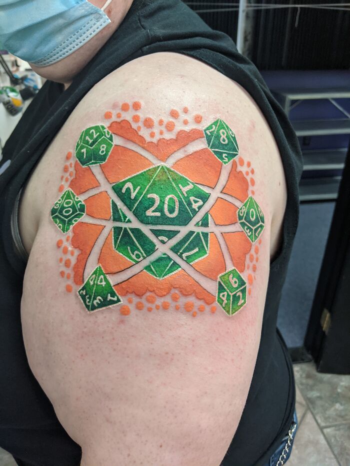 Colorful D20 dice tattoo on arm, featuring vibrant green and orange elements.