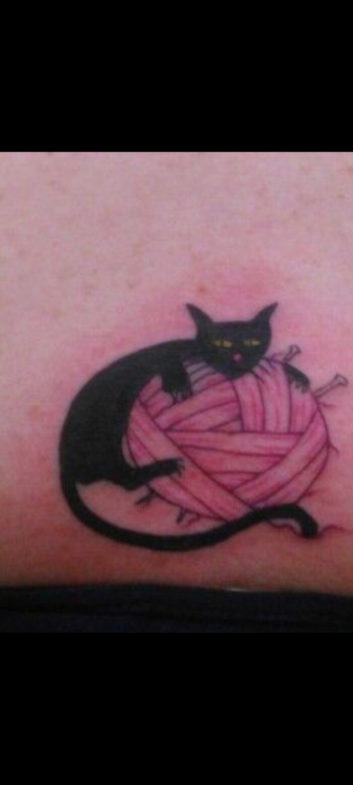 Tattoo of a black cat playing with a pink yarn ball.
