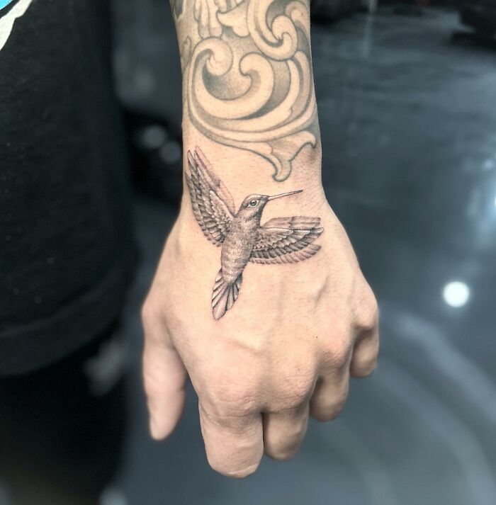 Tattoo of a hummingbird on a person's hand, showcasing intricate design and artistic flair.