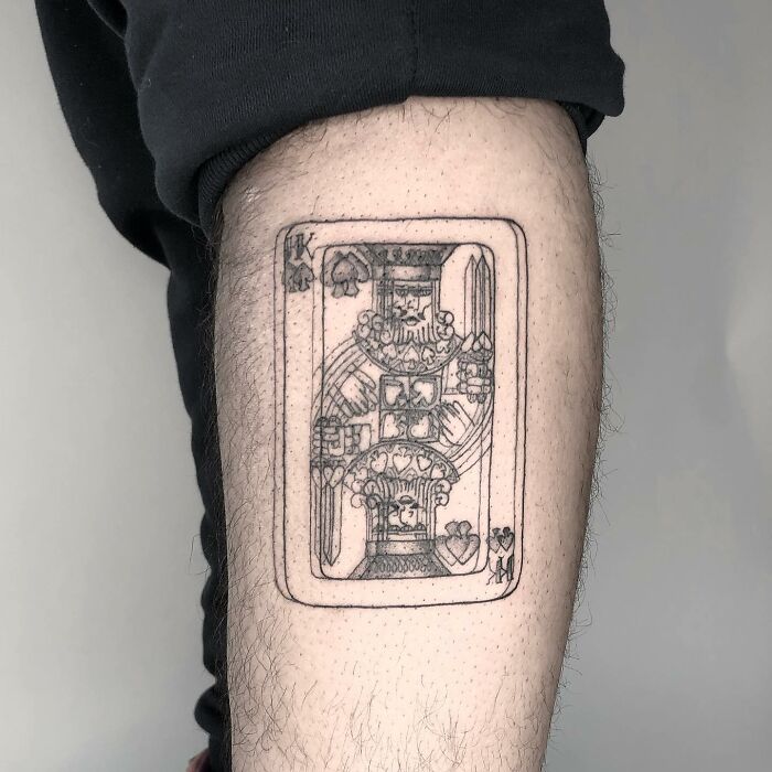 King of hearts tattoo on arm, showcasing detailed line work in a playing card design.
