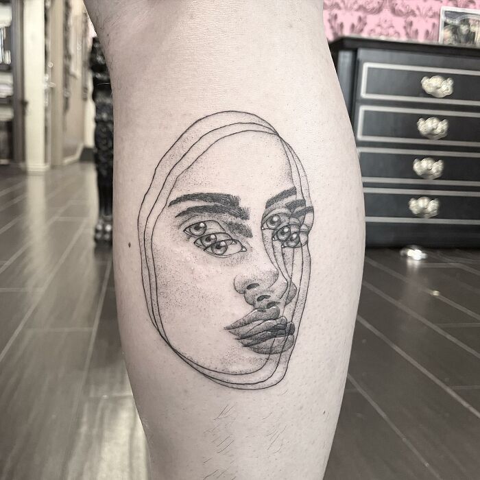 Abstract face tattoo with overlapping features on leg, showcasing a 'moving' visual effect in a modern design.