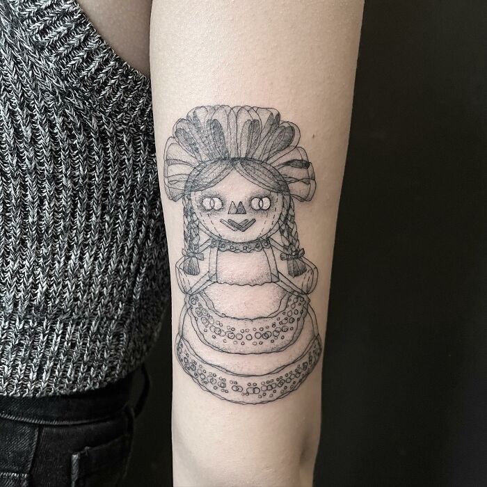 Tattoo of a detailed doll design on an arm, showcasing intricate linework, part of a series of moving tattoos.