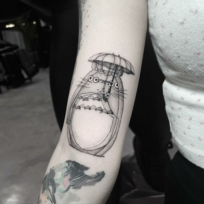 Tattoo of Totoro holding an umbrella on a forearm, showcasing moving tattoo artistry.