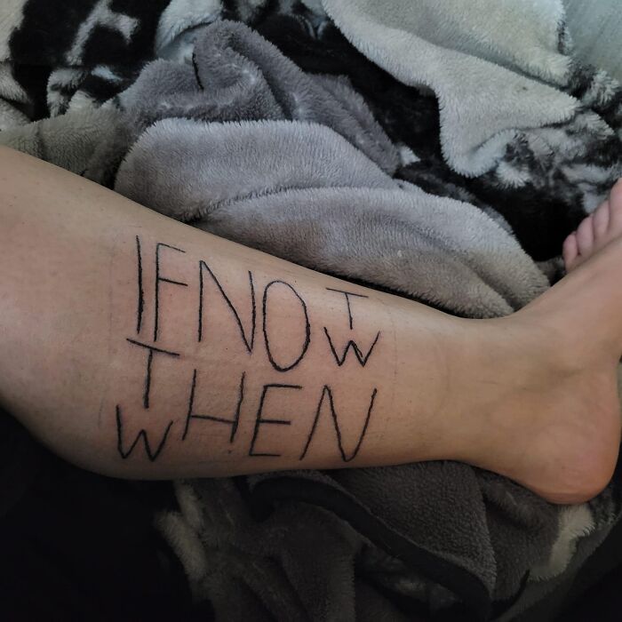 Bad tattoo reading "IF NOT WHEN" on a person's leg with blankets in the background.