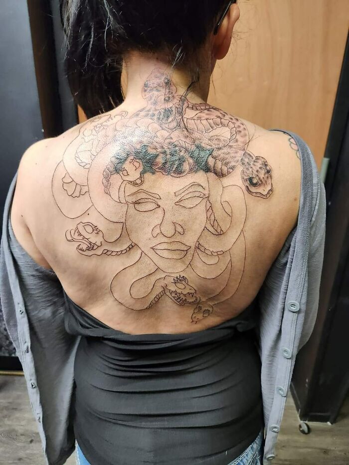 Bad tattoo of Medusa on woman's back, showcasing a hilariously unfinished design with snakes.