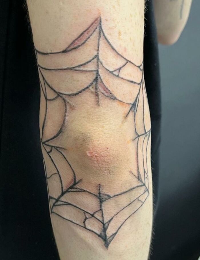 Bad tattoo of a spider web on an elbow, showcasing hilarious ink mishap.