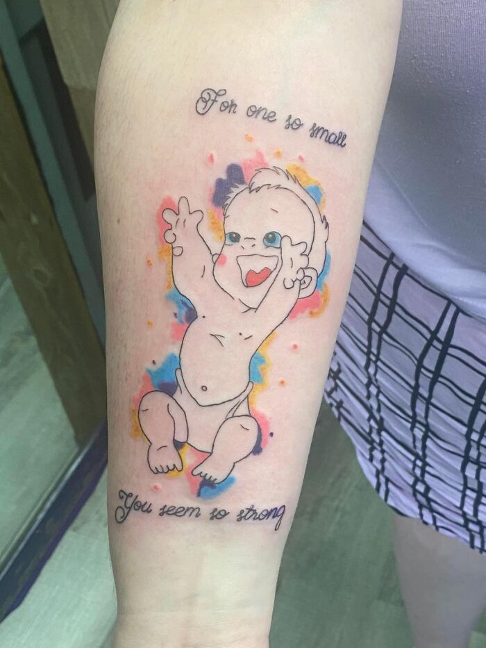 Bad tattoo of a baby with colorful background on arm, humorous text says "For one so small, you seem so strong."