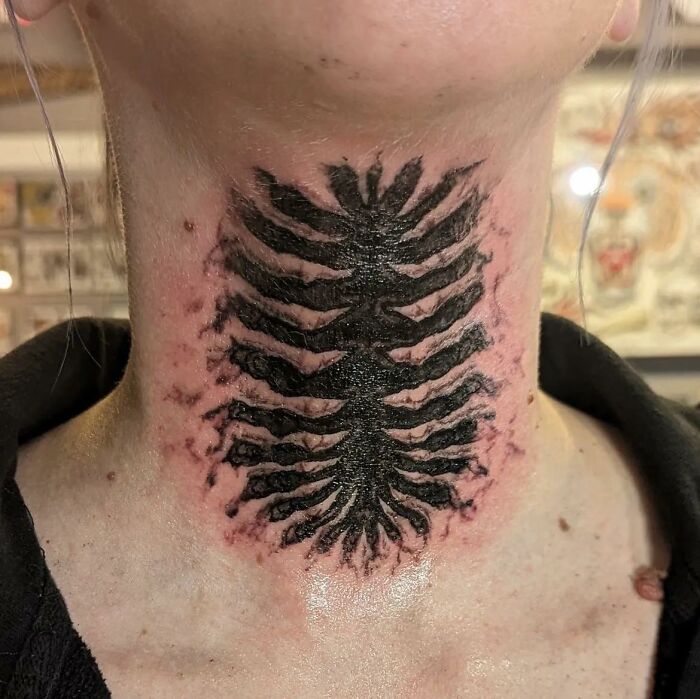 A person with a large, black tattoo resembling a fern on their neck, showcasing a hilariously bad tattoo.