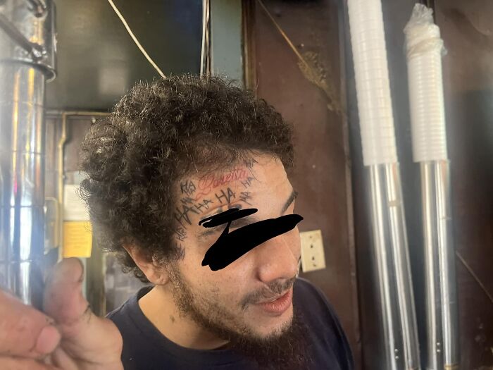 Man with amusingly bad forehead tattoo that reads "HA HA" in a casual indoor setting.