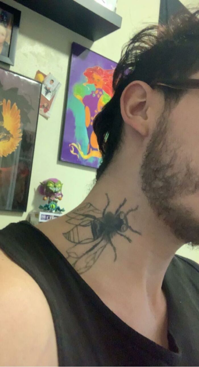 Neck tattoo of a large bee on a person, surrounded by art and decorations.
