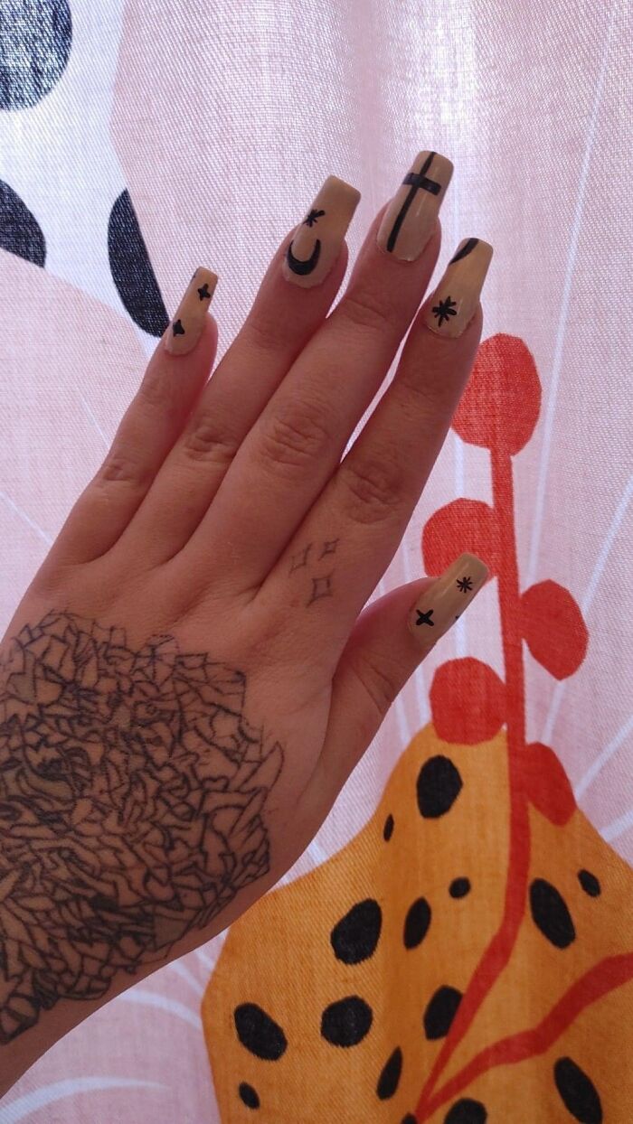 Hand with a hilariously bad tattoo and nails with uneven black symbols.
