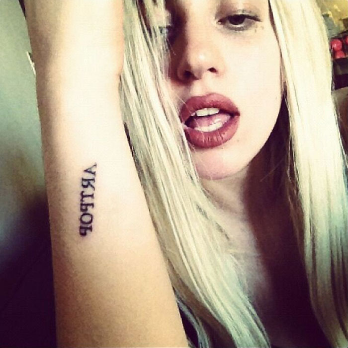 Celebrity showing an arm tattoo with mirrored letters, leaning towards the camera.