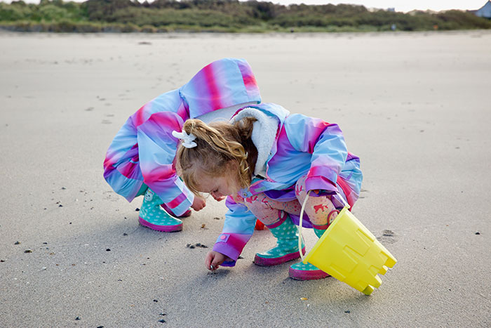 Girls holding yellow plastic bucket and collecting shells at the beach