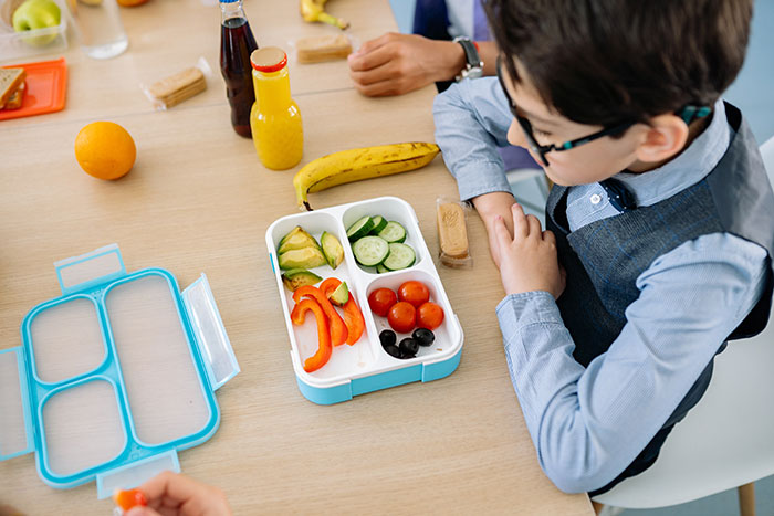 Boy in blue long sleeve shirt sitting on chair in front of table with lunch box