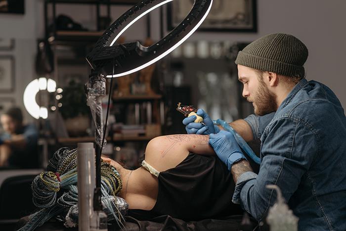 Tattoo artist working on client in studio under bright light.