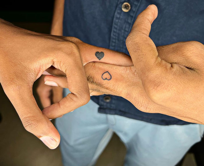 Matching heart tattoos on fingers, symbolizing a special bond for couples, siblings, or friends.