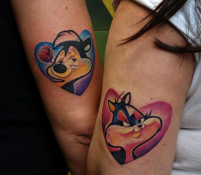 Matching tattoos on arms with cartoon characters inside heart shapes, symbolizing a special bond.