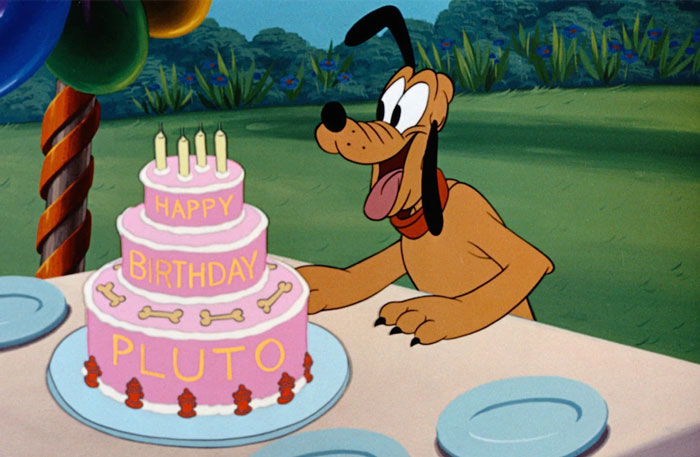 Cartoon dog celebrating a birthday with a pink cake outdoors.