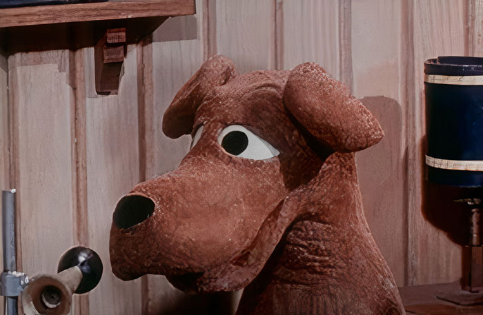 Claymation cartoon dog with a curious expression, featuring large eyes and textured fur, against a wooden backdrop.