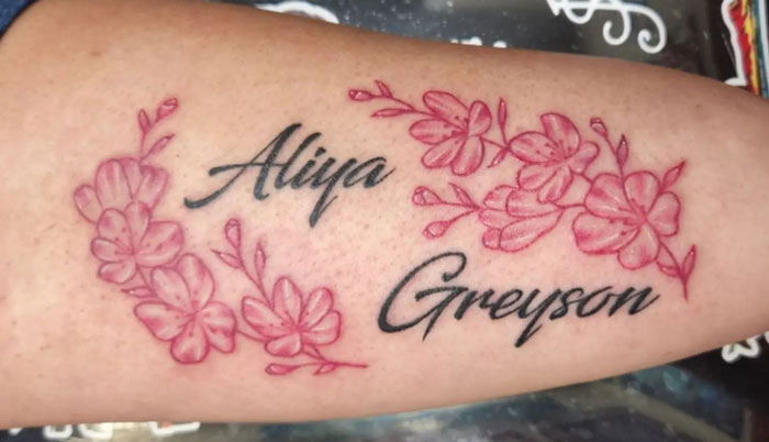 Floral tattoo with delicate pink blossoms and names "Aliya" and "Greyson" elegantly inked on the skin.