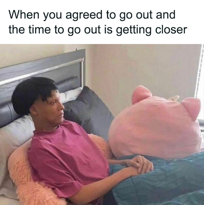Person sitting in bed with a worried expression, next to a large pink plushie, capturing relatable meme humor.