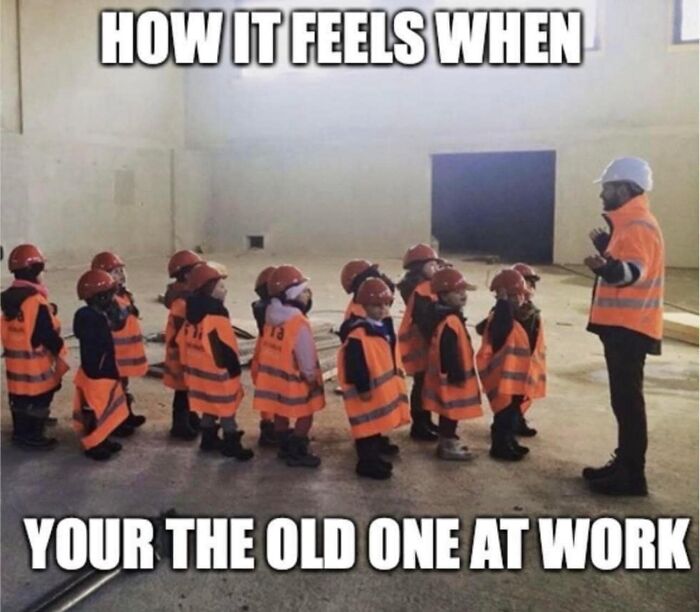 Children in construction vests and hard hats lined up humorously with an adult, illustrating office life dynamics.