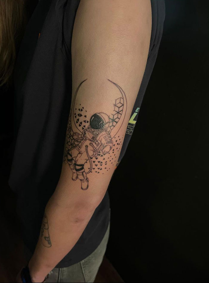 Geometric tattoo featuring an astronaut on a person's arm, showcasing intricate line work and creative design elements.
