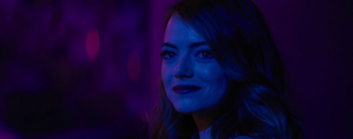 Actress in blue and purple lighting, smiling slightly while looking ahead, representing highest-paid actors.
