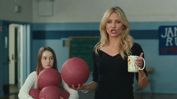 Actress holding a mug and talking in a gymnasium with a girl carrying multiple red balls, highlighting highest-paid actors.