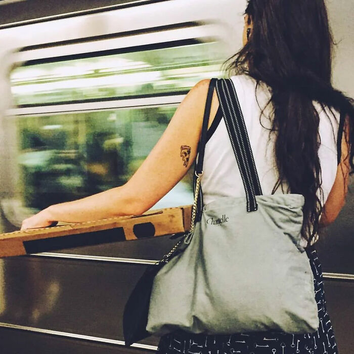 Person with a pizza slice tattoo carrying a pizza box on a subway train, perfectly matching the situation.
