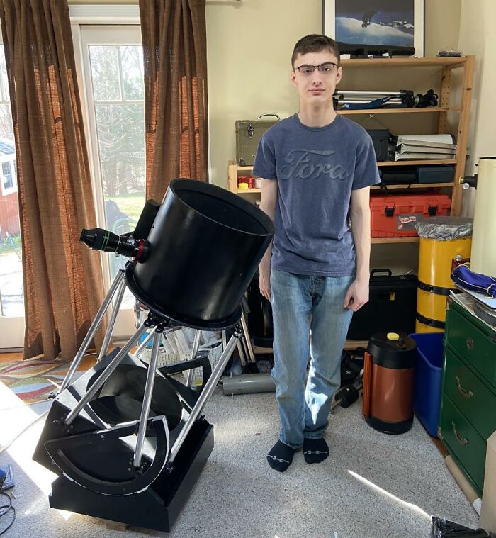 Boy standing next to a Newtonian reflector telescope