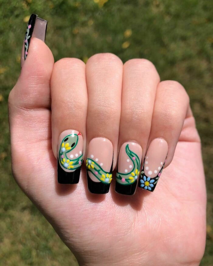 Nail art with floral designs on long nails, featuring black French tips and colorful accents.