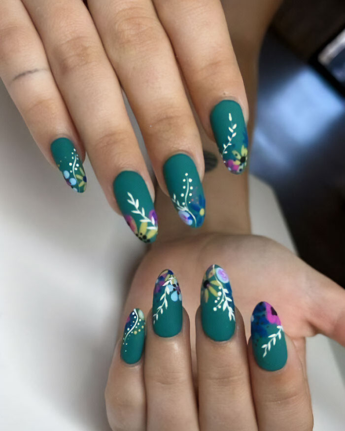 Colorful floral nail art with green and purple elements on long, painted nails.