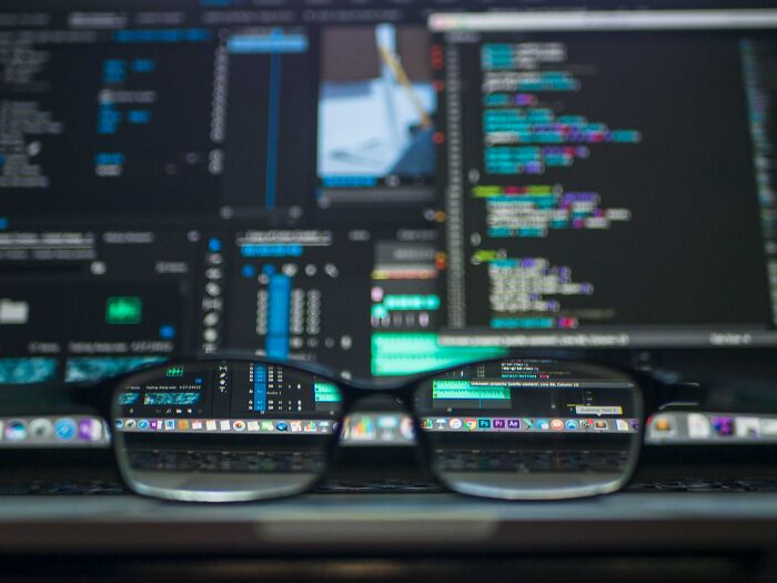Glasses On Table And Coding On Computer Screens 