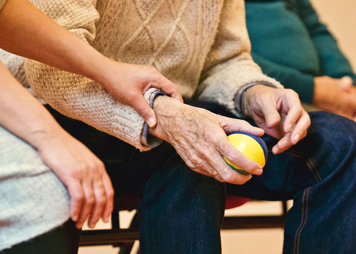 Elderly person holding a stress ball while someone offers comforting touch, capturing a moment of care and connection.