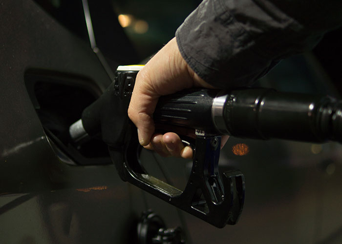 A hand holding a gas pump nozzle inserted into a car, illustrating a real and common danger discussed in scientific contexts.