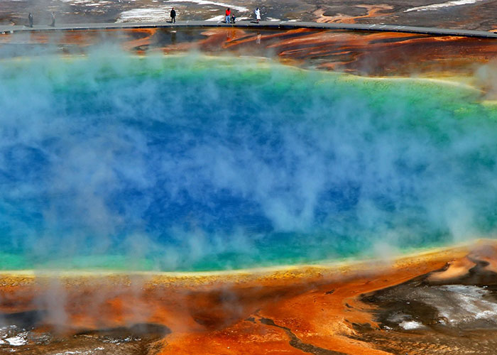 Colorful geothermal pool with steam, a real scientific phenomenon surrounded by tourists.